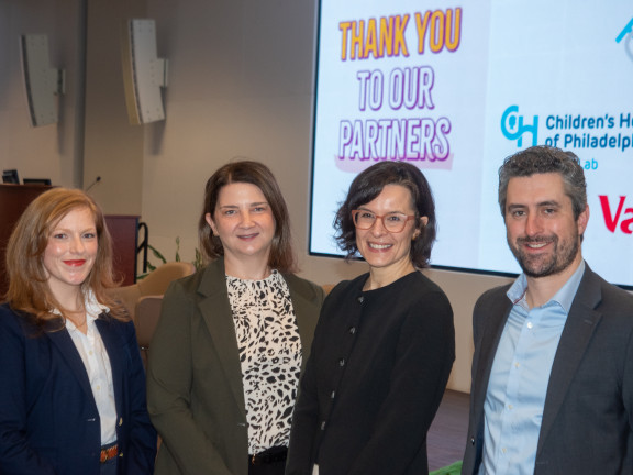 4 professionals stand smiling together in front of screen that says Thank You To Our Partners
