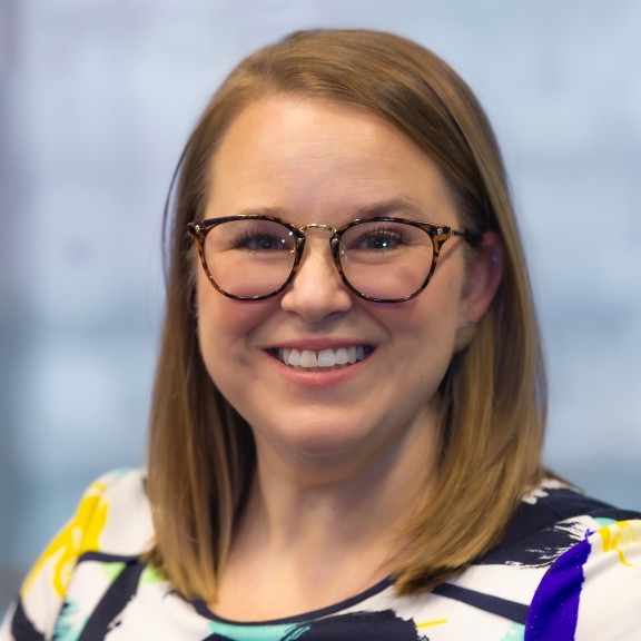 Blonde woman smiling and wearing glasses and a colorful top