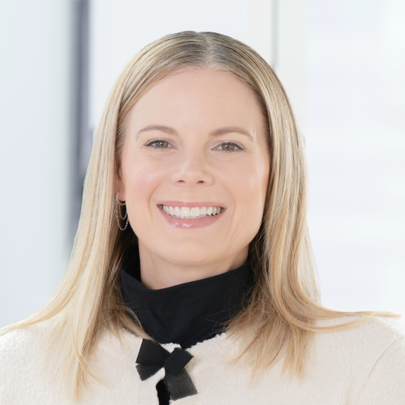 Headshot, Julia is wearing a black and white cardigan, hair is blonde and down to her shoulders. She is smiling