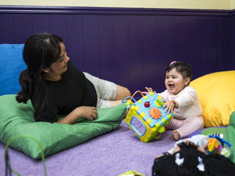 woman laying down and baby sitting and playing with toy