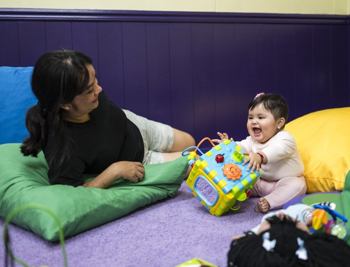woman laying down and baby sitting and playing with toy