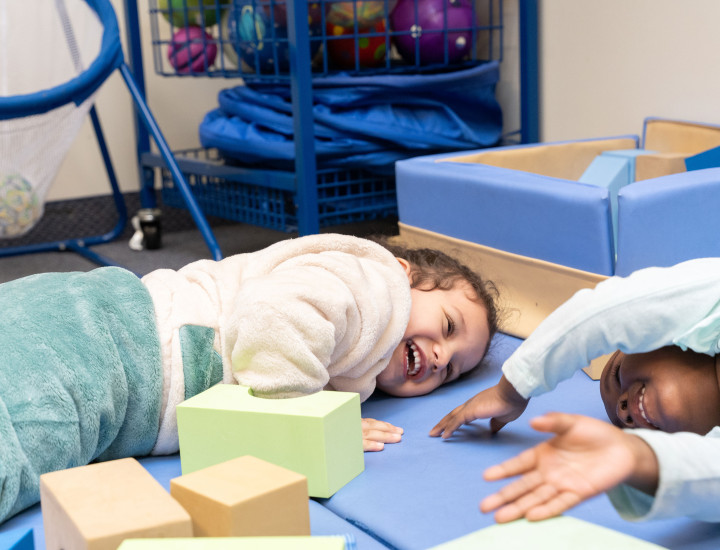 Two kids lay on mats smiling and laughing together